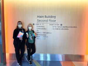 Two masked providers standing near hospital sign