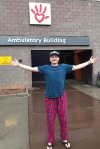 Teen standing with arms outstretched in front of hospital