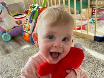Smiling toddler sitting on floor hugging stuffed Elmo doll