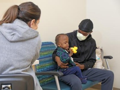 Masked father holding toddler in exam room