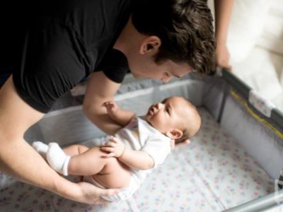 Father putting baby down into cot