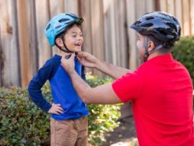 Parent adjusting bicycle helmet on boy