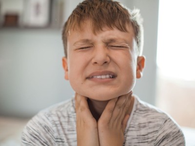 Kid wincing in pain, holding his throat