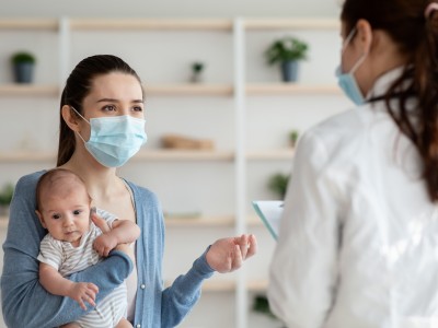 Mother holding infant, speaking to masked provider