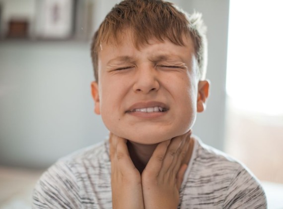 Kid wincing in pain, holding his throat