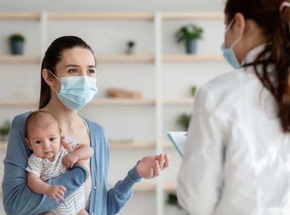 Mother holding infant, speaking to masked provider